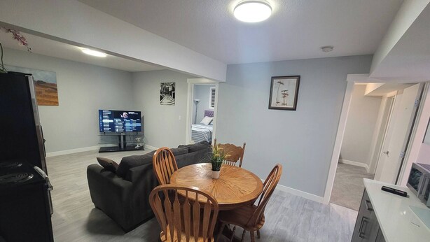 Una sala de estar moderna con una mesa de comedor, sillas, un sofá, un televisor y una zona de cocina.