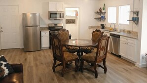 A compact kitchen with a refrigerator, microwave, oven, and dishwasher. There is a dining table with four chairs. The kitchen has white cabinets and a wooden floor. - Saddle Up at Rodeo Ranch House! Cowboy Vibes, Blocks from the Stockyards Action! (Fort Worth)