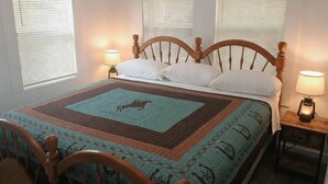 A bedroom with a wooden bed, white bedding, and a quilt with a horse design. There are three windows with blinds, and two bedside lamps. - Saddle Up at Rodeo Ranch House! Cowboy Vibes, Blocks from the Stockyards Action! (Fort Worth)
