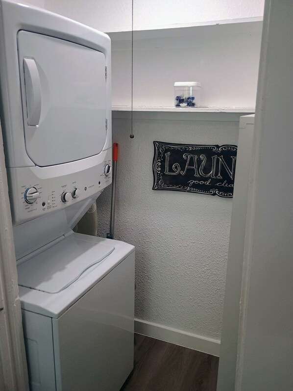 Une petite buanderie équipée d’un lave-linge et d’un sèche-linge à chargement frontal, d’une petite étagère avec un récipient et d’une décoration murale.