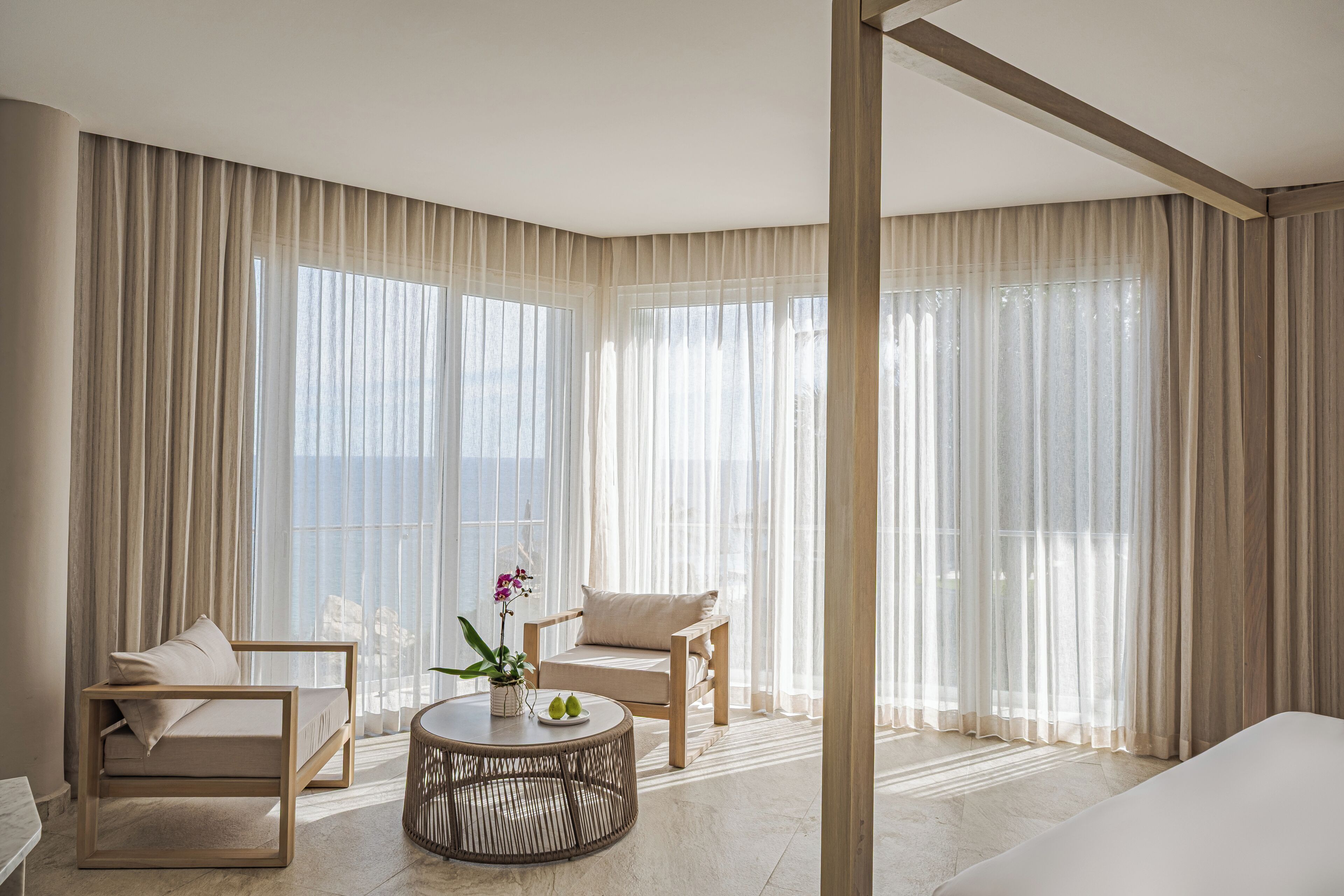 A modern hotel room with a large window, a sofa, a chair, and a round coffee table.