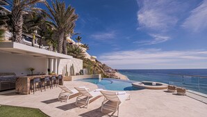 Ein Poolbereich mit Liegestühlen, einer Bar und Blick auf den Ozean.