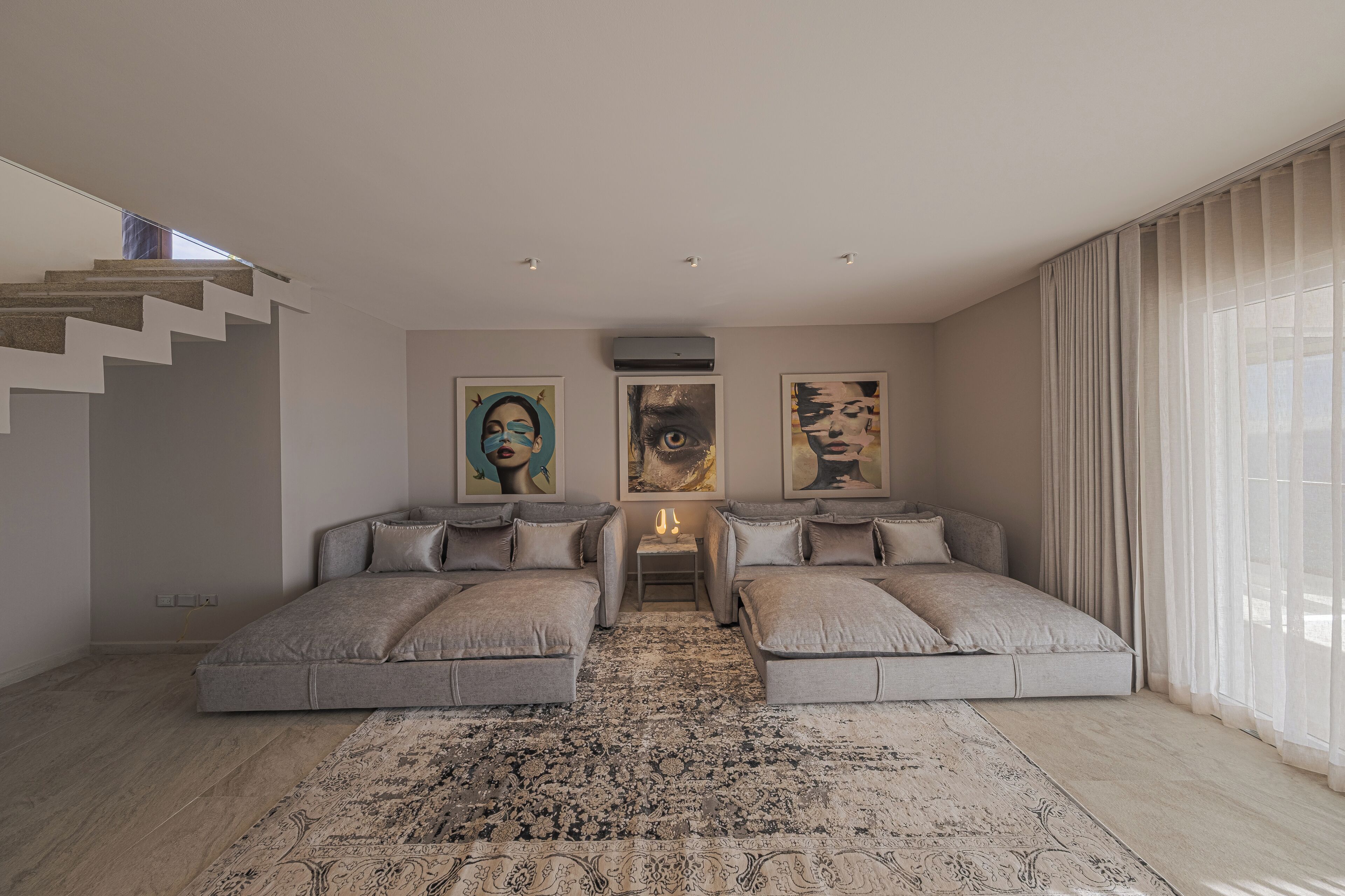 A modern bedroom with a central sofa bed, a large rug, and artwork on the walls.