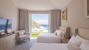 Ein Hotelzimmer mit einem großen Bett, einer Couch, einem Fernseher und Blick auf Strand und Meer.
