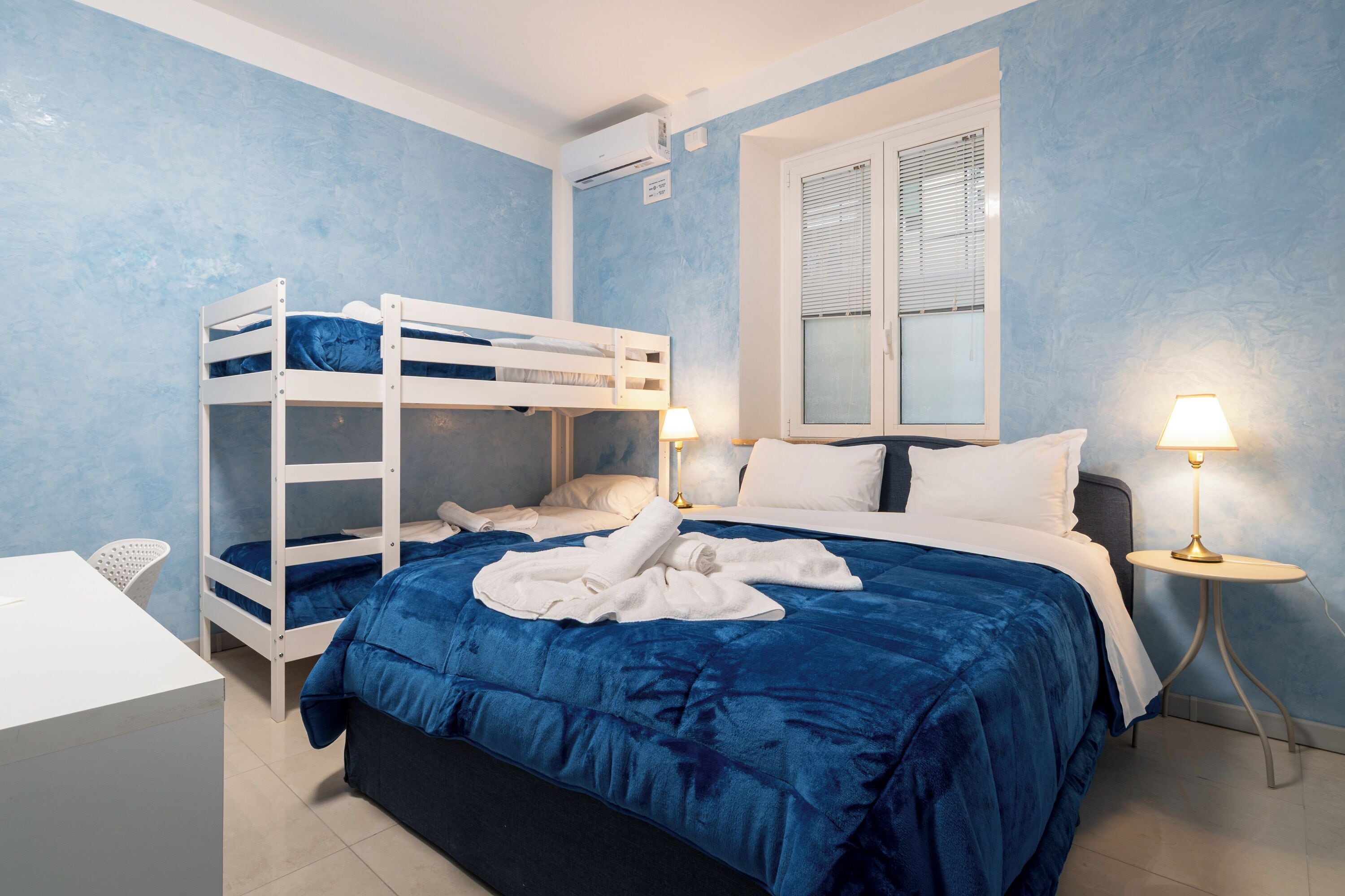 A bedroom with bunk beds, a desk, and bedside lamps.