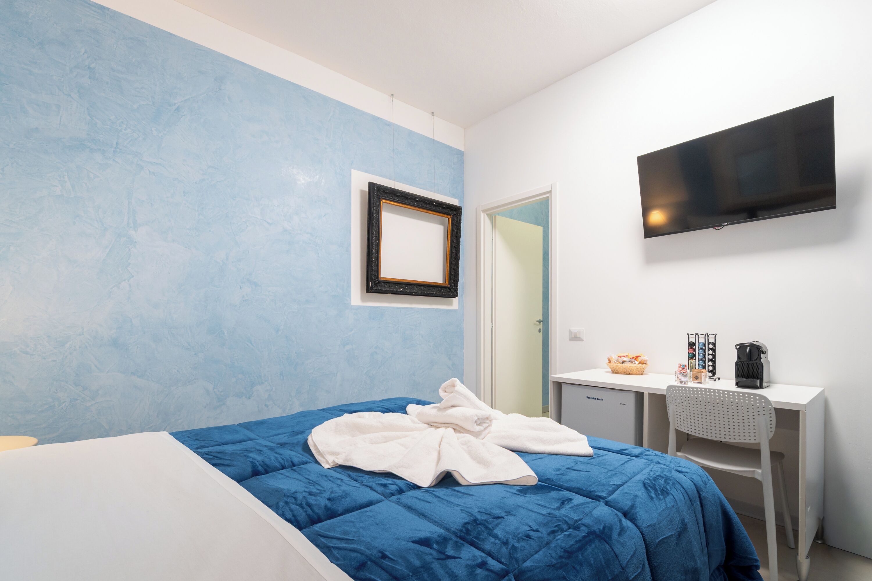 Habitación de hotel con cama, escritorio, silla, televisión y una pequeña zona de kitchenette.
