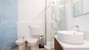Et moderne badeværelse med toilet, bidet og en brusekabine i glas.