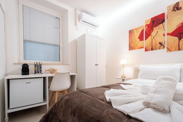 A hotel room with a bed, a desk with a computer, a small fridge, and a window with blinds. - Vitti's home Verona 6 (Verona)