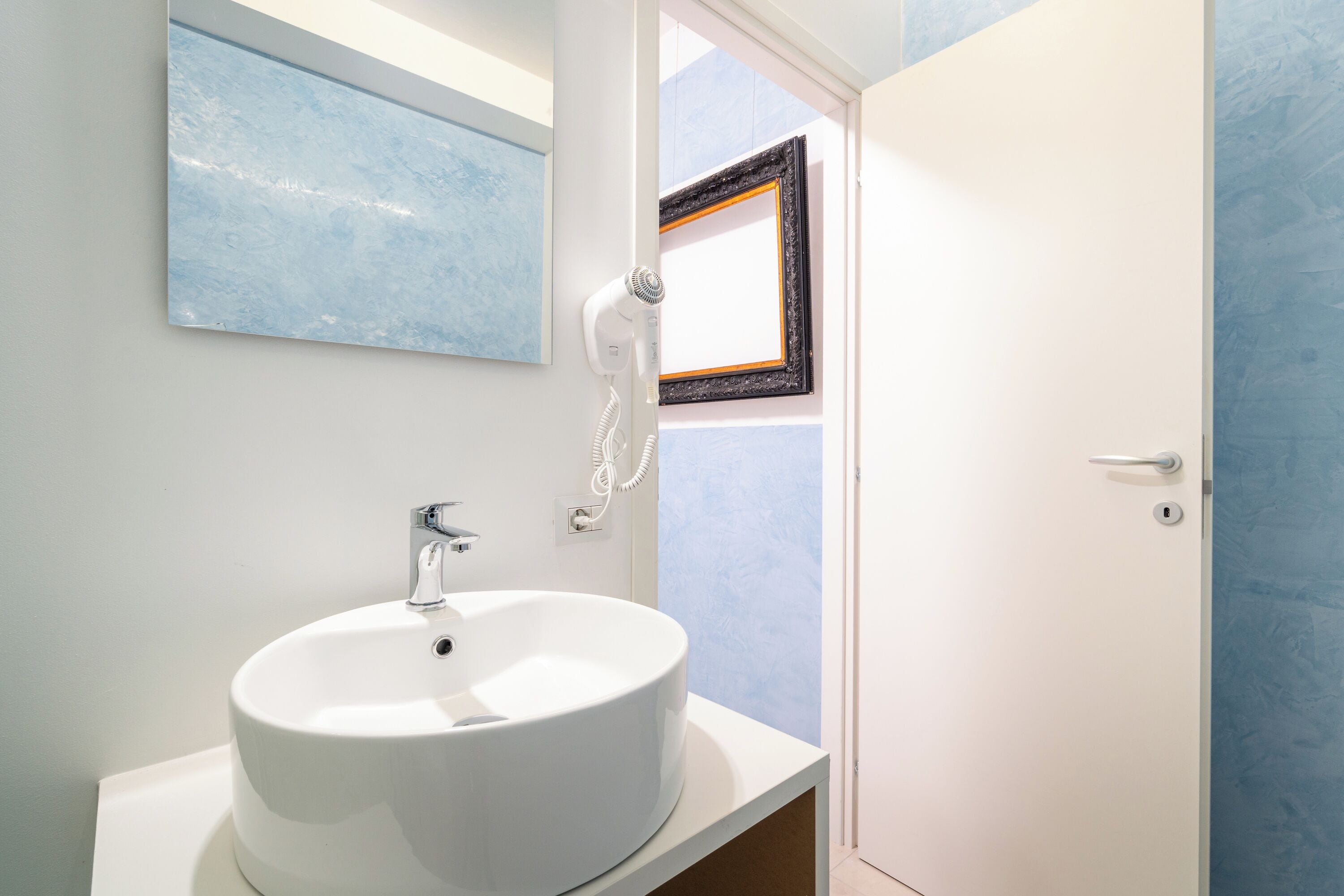 A bathroom with a white sink, a hairdryer, and a framed picture on the wall.
