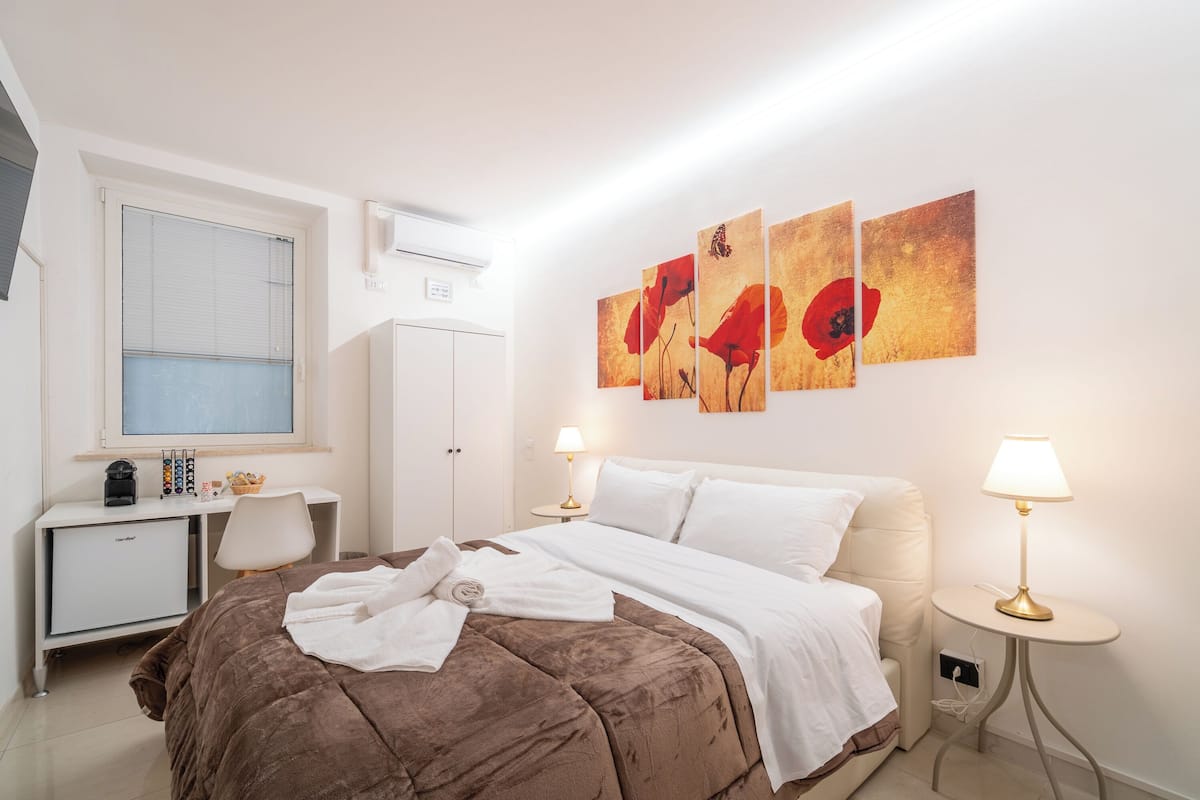 Habitación de hotel con cama, lámparas de noche, un escritorio con computadora y una ventana con persianas.