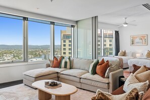 A modern hotel room with a large window, a sofa, a bed, and a ceiling fan. - Level 18 City View Private Apartment (Surfers Paradise)