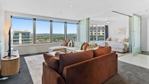 Ein geräumiges Wohnzimmer mit großem Fenster, einer Couch, einem Couchtisch und einem Bett im Hintergrund.