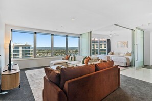 A spacious living room with a large window, a sofa, a coffee table, and a bed in the background. - Level 18 City View Private Apartment (Surfers Paradise)