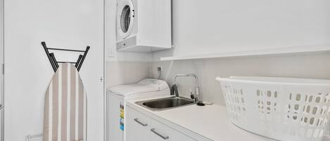 A compact laundry area with a washing machine, a drying rack, a sink, and a laundry basket.