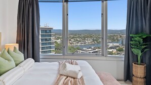 Ein Hotelzimmer mit großem Fenster und Blick auf die Stadt, einem ordentlich bezogenen Bett und einer Zimmerpflanze.
