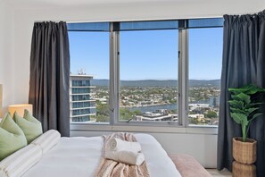 A hotel room with a large window offering a city view, a neatly made bed, and a potted plant. - Level 18 City View Private Apartment (Surfers Paradise)