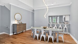 A dining area with a round table and white chairs, a wooden dresser, and a pendant light. - Sun Sand Repeat - Modern Coastal Townhome in Gulf Place (Santa Rosa Beach)