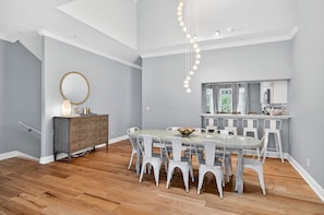 A dining area with a round table and white chairs, a wooden dresser, and a pendant light. - Sun Sand Repeat - Modern Coastal Townhome in Gulf Place (Santa Rosa Beach)