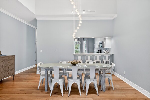 A dining area with a round table, white chairs, and a chandelier. - Sun Sand Repeat - Modern Coastal Townhome in Gulf Place (Santa Rosa Beach)