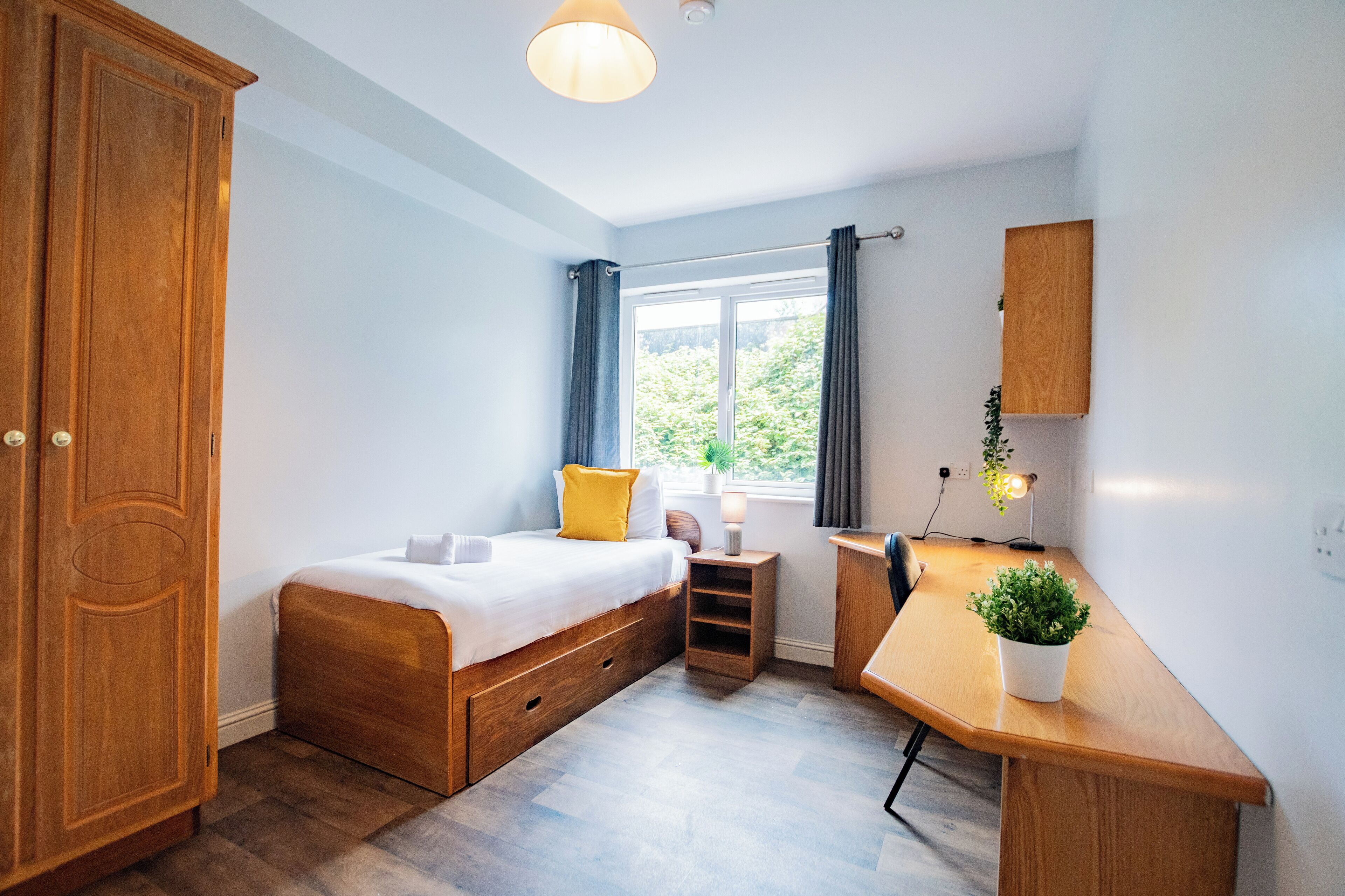 A bedroom with a wooden bed, a desk, a wardrobe, and a window with curtains.