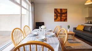 A dining area with a table set for six, wooden chairs, a sofa, and a TV in the background. - Family & Group-Friendly Galway Apartment (Galway)