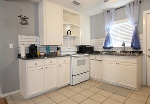 A kitchen with white cabinets, a double oven, a coffee maker, and a window with blue curtains.
