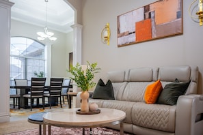 Un salon avec un canapé beige, une table basse ronde et un coin repas comprenant une table et des chaises.