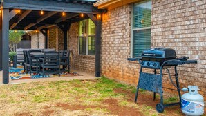 An outdoor patio with a grill, seating, and a gas tank. - Hill Country | Spacious 4BR Retreat (Abilene)