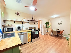 A kitchen with a microwave, coffee maker, and oven. There is a dining table with chairs and a plant.