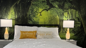 A bed with a forest-themed wallpaper, two bedside lamps, and two pillows with text. - Raptor Ridge - Your Abilene Adventure Basecamp (Abilene)