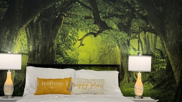 A bedroom with a forest-themed wallpaper, a bed with white bedding, two bedside lamps, and two pillows with text. - Raptor Ridge - Your Abilene Adventure Basecamp (Abilene)