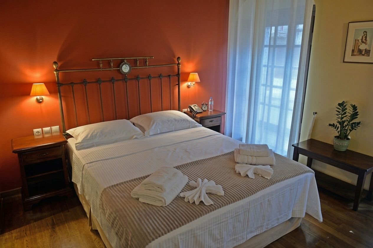 Ein Hotelzimmer mit einem Bett, zwei Nachttischlampen, einem Nachttisch, einem kleinen Tisch mit einer Pflanze und einem Fenster mit Vorhängen.