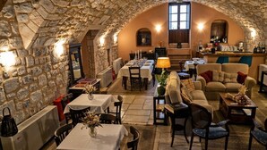 Un comedor acogedor con paredes y techo de piedra, y una zona de bar con mostrador y taburetes. Las mesas están preparadas con manteles blancos y velas.