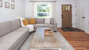 Un salon avec un canapé, une table basse, une porte et une fenêtre avec des rideaux.