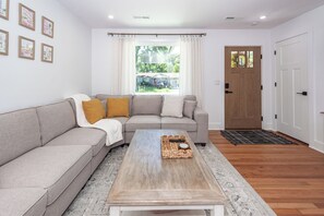 Ein Wohnzimmer mit einer Couch, einem Couchtisch, einer Tür und einem Fenster mit Vorhängen.