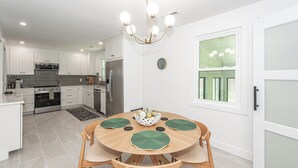 Une cuisine moderne avec des meubles blancs, des appareils en acier inoxydable et un coin repas comprenant une table ronde et des chaises.