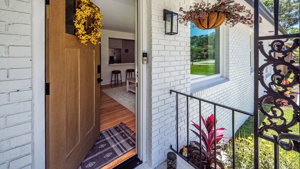 Un intérieur moderne avec un mur en briques blanches, une porte en bois, un coin cuisine et un balcon agrémenté de plantes.