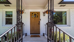 Une maison en briques blanches avec une porte d’entrée en bois, le numéro « 3142 » au-dessus de la porte et un escalier en métal menant à l’entrée.