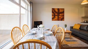 A dining area with a table set for six, wooden chairs, a sofa, and a TV in the background. - Comfort, Space & Value Galway Apartment (Galway)