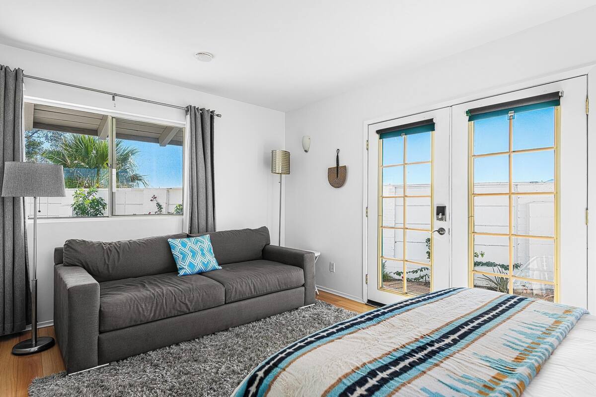 Une chambre moderne avec un canapé gris, une couvre-lit à motifs et une vue à travers une porte vitrée.