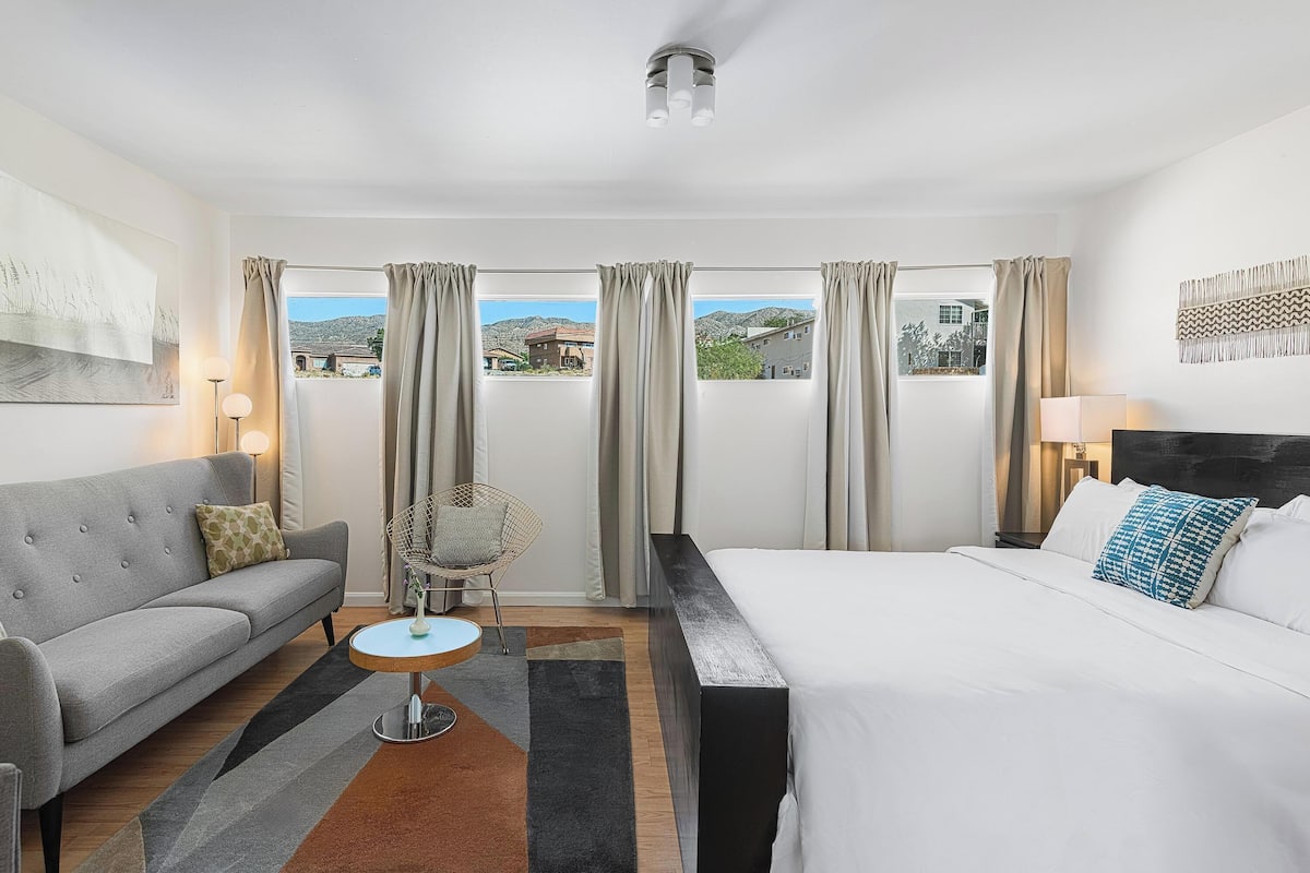 Une chambre d’hôtel avec un lit, un canapé, une chaise, une petite table et une vue sur l’extérieur.