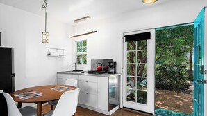 Eine moderne Küche mit Esstisch, Stühlen, einem Wasserkocher und Blick auf den Garten durch eine Glastür.