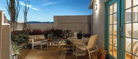 A patio with a table and chairs, surrounded by potted plants and a sofa.