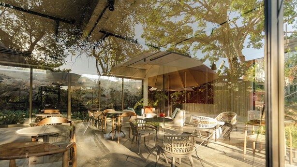 An outdoor seating area with tables and chairs, large windows, and a view of trees and rocks.