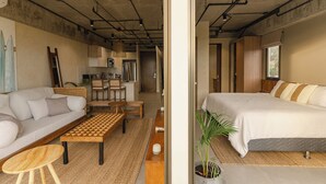 A modern interior with a sofa, a wooden coffee table, a bed, and a kitchen area visible through an open doorway.