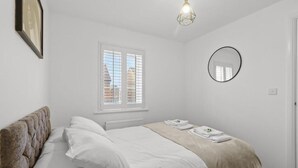 Ein Schlafzimmer mit Bett, Fenster, Spiegel und einer Pendelleuchte.