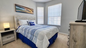Un dormitorio con cama, mesitas de noche, lámpara, escritorio y ventana.