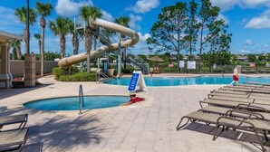 Un área de piscina con tobogán de agua, sillas de descanso y palmeras.