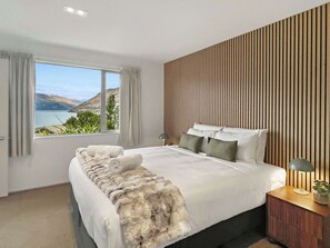 A modern bedroom with a large bed, a view of the outdoors, and a wooden panel wall.