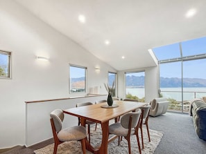 A modern dining area with a wooden table and chairs, large windows with mountain views, and a cozy seating area with a blue sofa.